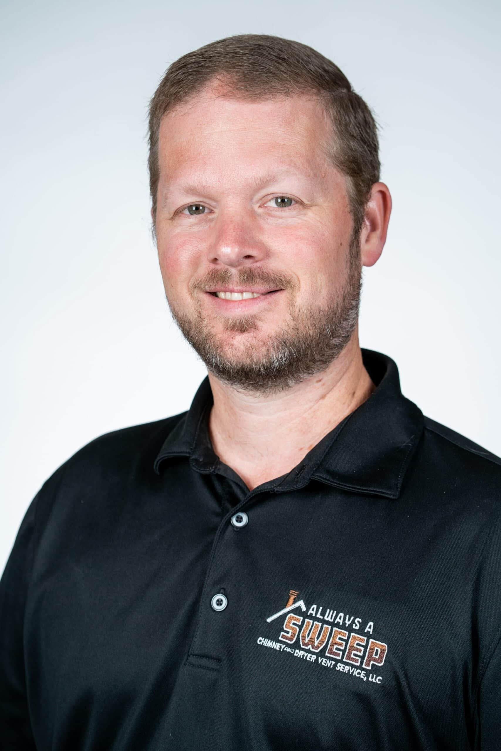 A professional headshot of a smiling man with a beard wearing a black polo shirt featuring the "Always A Sweep Chimney and Dryer Vent Service" logo.