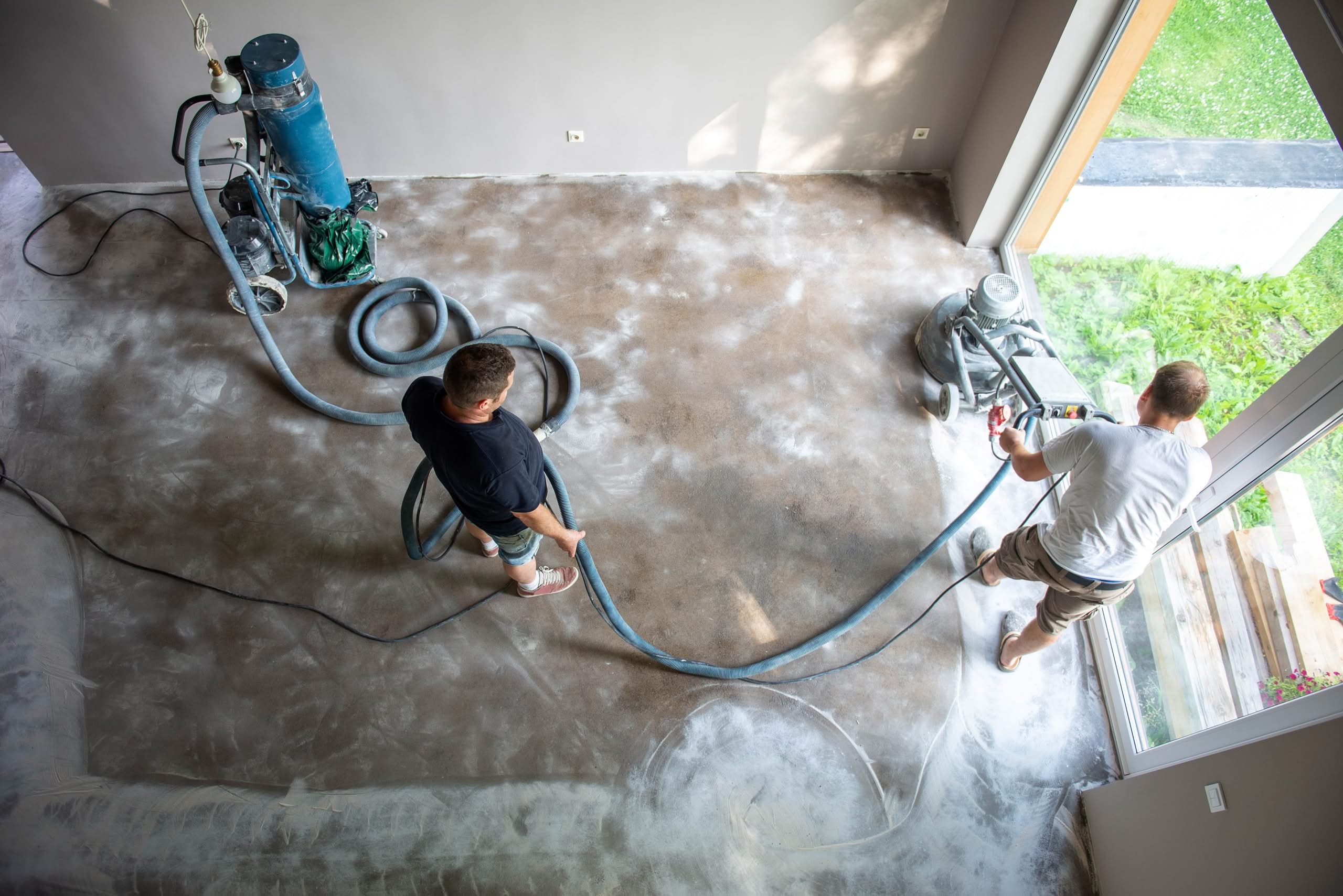 Water Damage Restoration in The Villages 1 Overhead view of two contractors using a professional floor grinder and a dust extraction vacuum system on a concrete floor in a residential space.