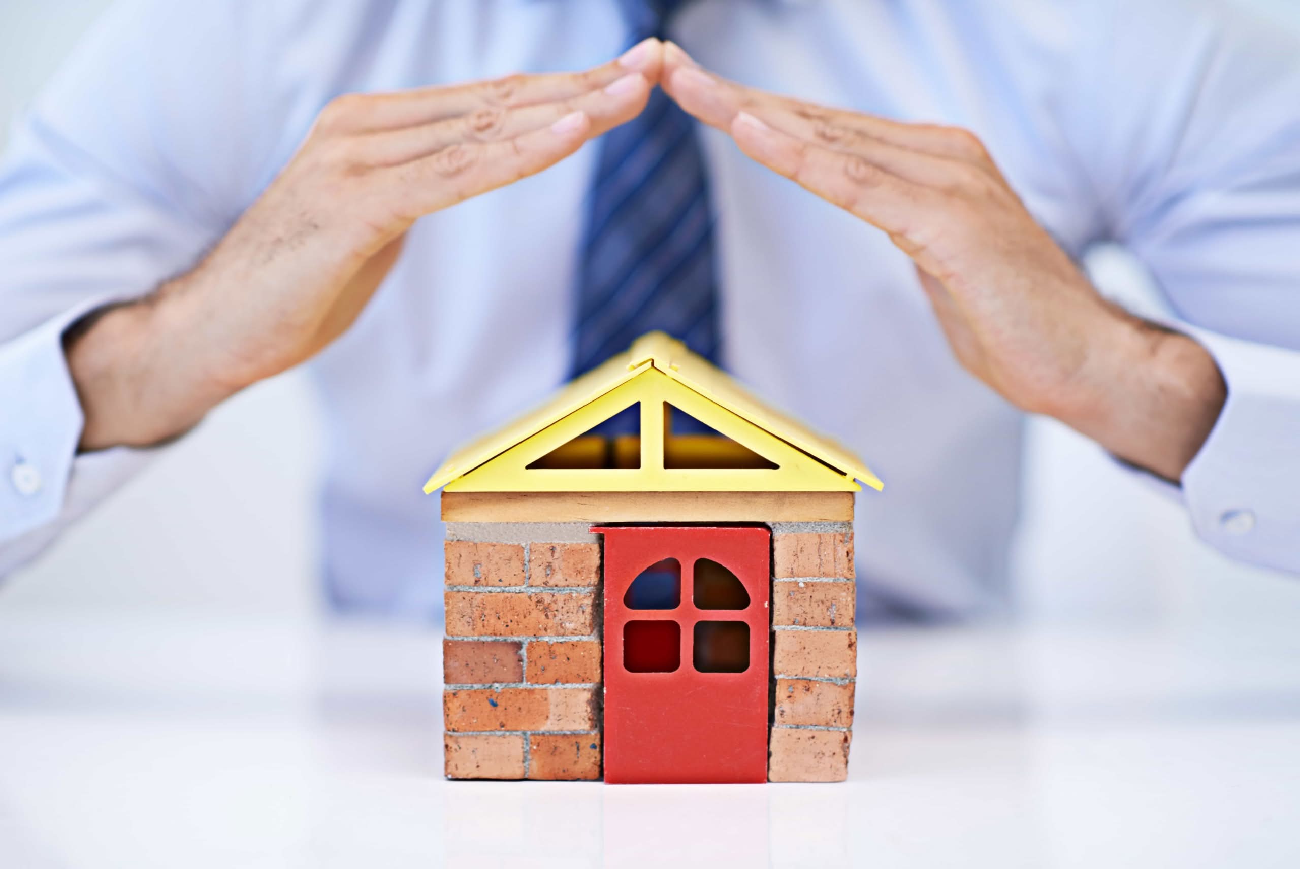A man in professional attire protecting a small model house with his hands, symbolizing residential asset protection. Expert home insurance service in Jacksonville, Florida.